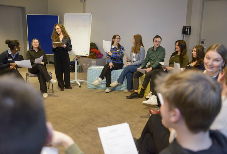The trainees sit in a large circle of chairs while planning the trainee day.