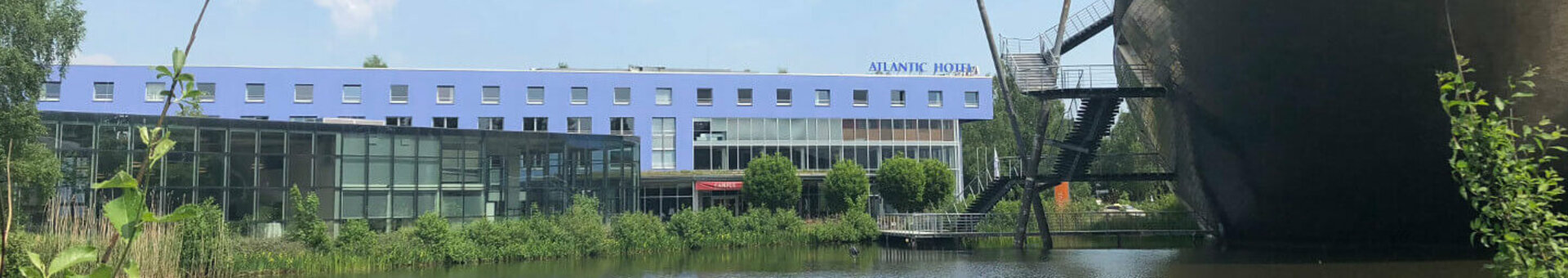 ATLANTIC Hotel Universum in Bremen, modern building on the waterfront, blue sky, green vegetation in the foreground.