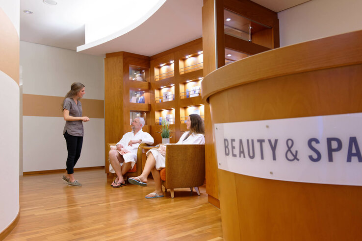 Hotel spa lounge with two guests in bathrobes being advised by a member of staff.