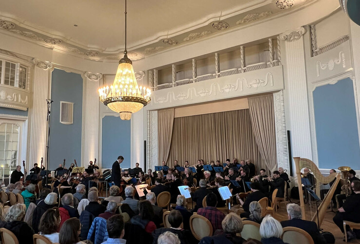 Konzert im prunkvollen Saal des ATLANTIC Grand Hotel Travemünde mit Orchester und Publikum unter großem Kronleuchter.