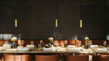 Elegantes Restaurant mit gedecktem Holztisch, Ledersesseln und Blumenvasen im ATLANTIC Hotel Münster.