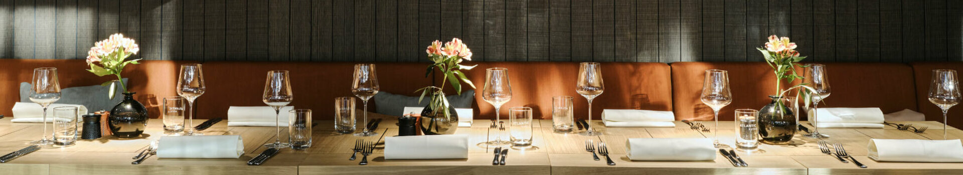 Elegantes Restaurant mit gedecktem Holztisch, Ledersesseln und Blumenvasen im ATLANTIC Hotel Münster.