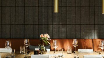 Elegantes Restaurant mit gedecktem Holztisch, Ledersesseln und Blumenvasen im ATLANTIC Hotel Münster.