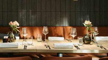 Elegantes Restaurant mit gedecktem Holztisch, Ledersesseln und Blumenvasen im ATLANTIC Hotel Münster.