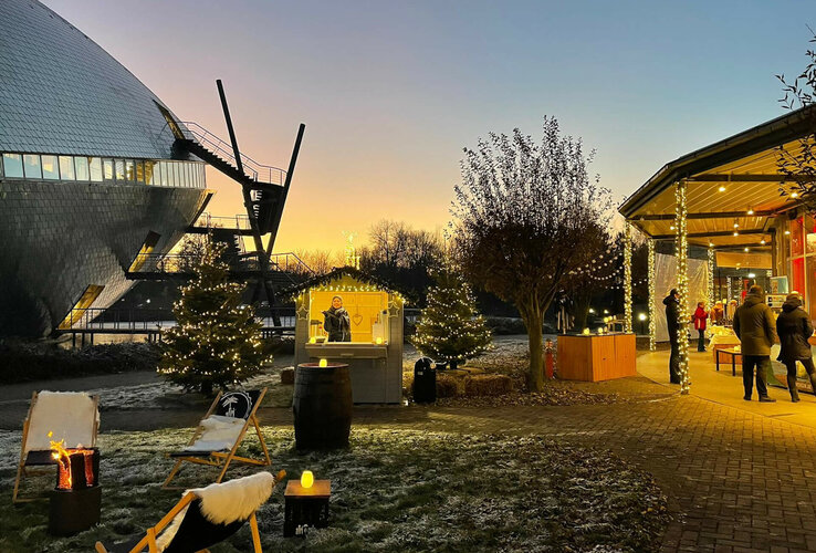 Weihnachtlich geschmückter Außenbereich des ATLANTIC Hotel Universum bei Sonnenuntergang, mit Lichterketten und Ständen.