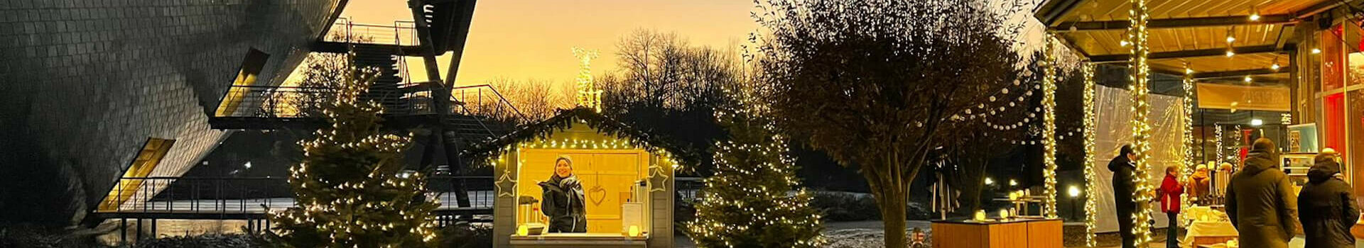 Weihnachtlich geschmückter Außenbereich des ATLANTIC Hotel Universum bei Sonnenuntergang, mit Lichterketten und Ständen.