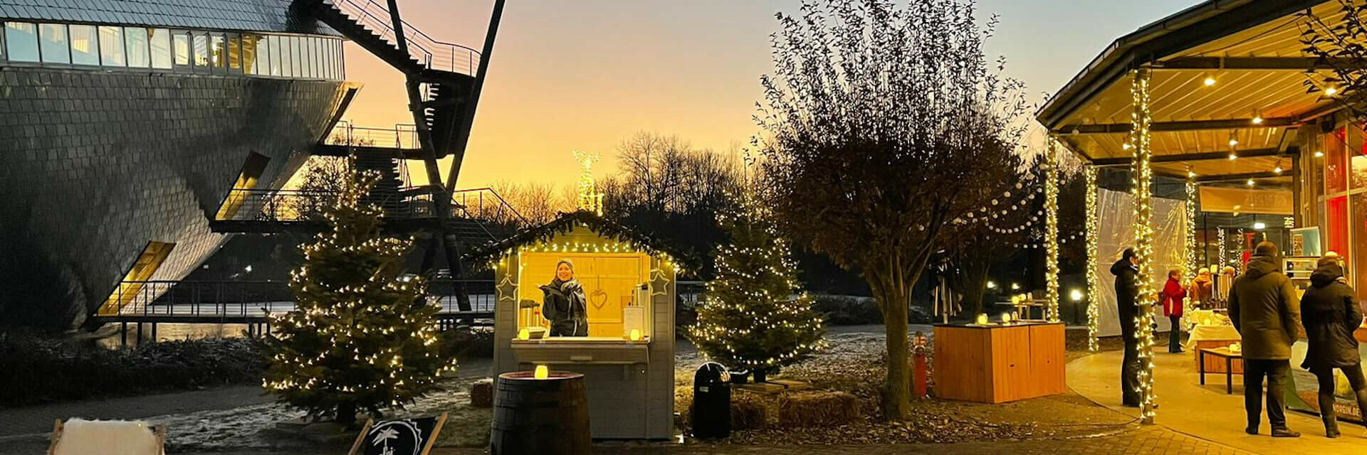 Weihnachtlich geschmückter Außenbereich des ATLANTIC Hotel Universum bei Sonnenuntergang, mit Lichterketten und Ständen.