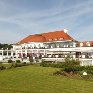 ATLANTIC Grand Hotel Travemünde with red roof, white facades, terrace and well-tended garden in the foreground.