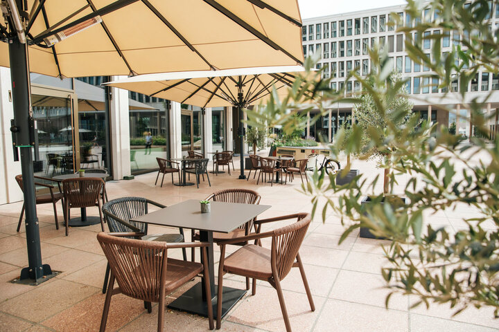 Die Terrasse der Deli Lounge mit beigen Sonnenschirmen und mehreren Tischen