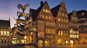 Bronzestatue der Bremer Stadtmusikanten vor historischen Gebäuden im Abendlicht.