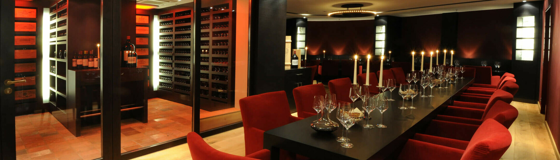 Tafel zur Weinprobe im Weinkeller des ATLANTIC Grand Hotel Bremen Eleganter Weinkeller mit langem Tisch, roten Stühlen und Kerzen im ATLANTIC Grand Hotel Bremen.