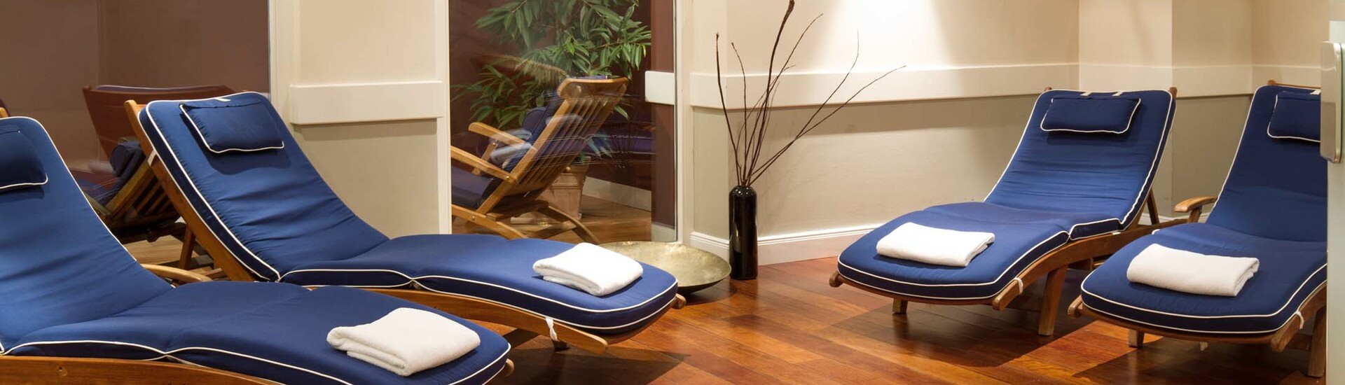 Ruhebereich mit Solarium im ATLANTIC Grand Hotel Travemünde Entspannungsbereich mit blauen Liegen, Holzboden und Pflanzen im ATLANTIC Grand Hotel Travemünde.