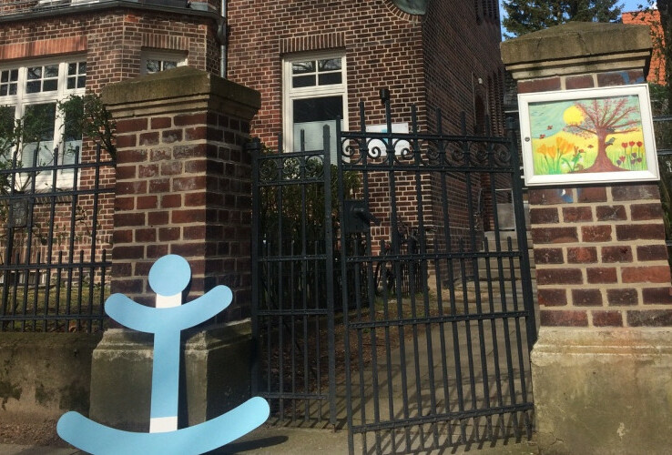 Ein Backsteingebäude mit einem schmiedeeisernen Tor und einem blauen Anker-Symbol davor.