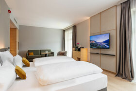 Modernes Hotelzimmer mit Doppelbett, Sofa, Flachbild-TV und großen Fenstern im ATLANTIC Hotel Heidelberg.