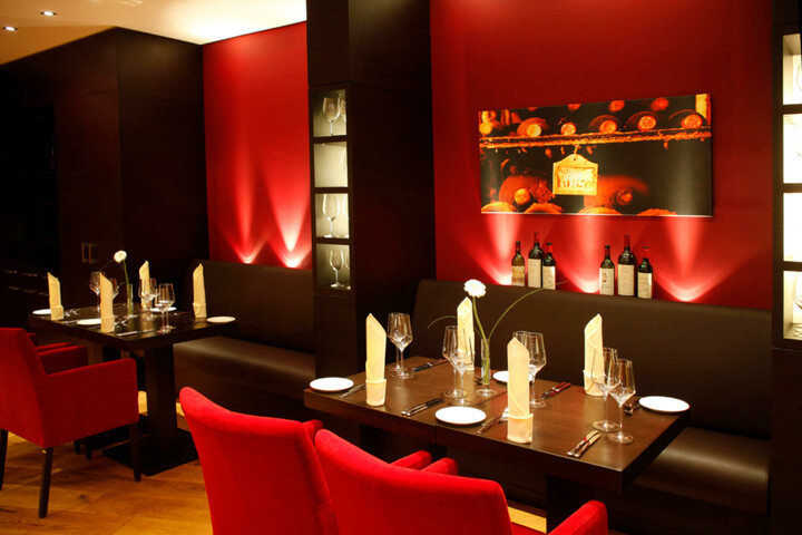 Gemütliches Hotelrestaurant mit roten Wänden, gedeckten Tischen, roten Stühlen und Weinflaschen als Dekoration.