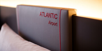 Nahaufnahme eines Betthaupts mit rotem "ATLANTIC Airport" Schriftzug im ATLANTIC Hotel Airport Bremen.