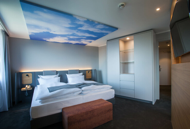 Modern hotel room with double bed, canopy motif on the ceiling, wardrobe, flat screen TV and bench in the ATLANTIC Hotel.