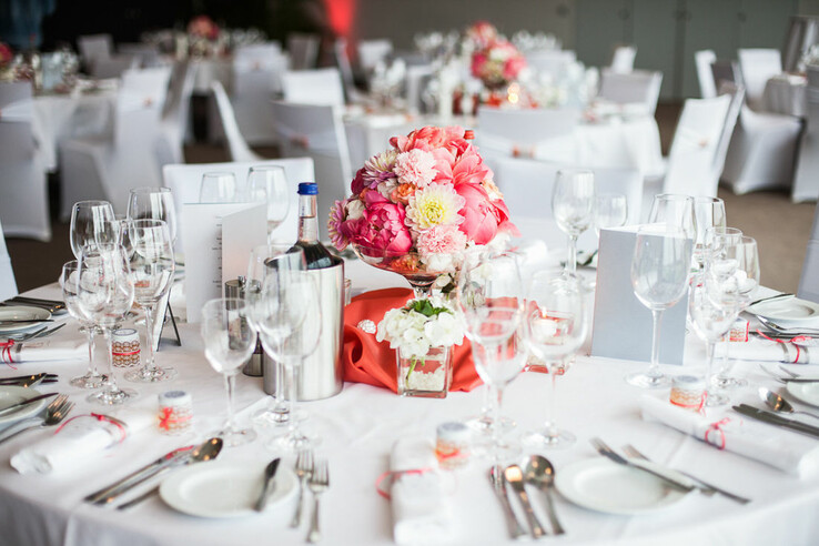 Festlich gedeckter Tisch mit weißen Tischdecken, Blumenarrangement und Weingläsern im ATLANTIC Hotel Galopprennbahn.
