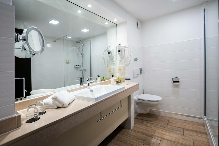 Modernes Hotelbad mit großem Spiegel, Waschbecken, Handtüchern, Dusche und WC, in hellen Farben gestaltet.