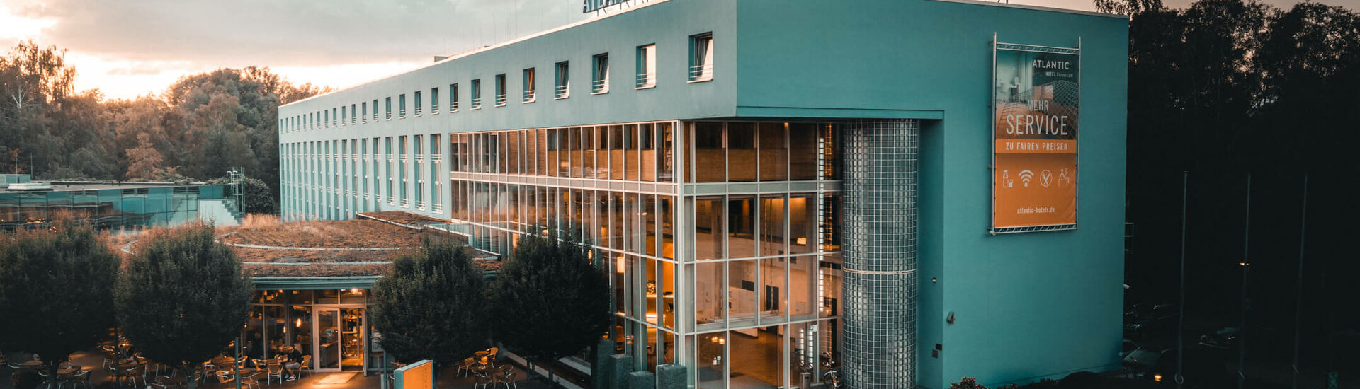 Exterior view l ATLANTIC Hotel Universum Bremen ATLANTIC Hotel Universum in Bremen, modern facade at sunset, with illuminated entrance and surrounding nature.