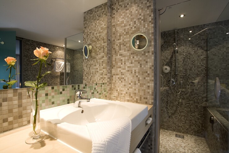 Modernes Badezimmer mit Mosaikfliesen, Waschbecken, Dusche und Vase mit Rosen im ATLANTIC Hotel Universum Bremen.