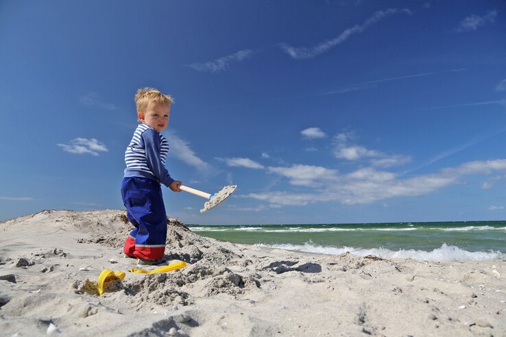 Kleinkind spielt mit Schaufel am Strand vor blauem Himmel am Ostseestrand Travemünde.