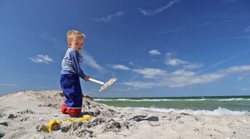 Kleiner Junge buddelt mit seiner Schaufel im feinen Ostseesand Kleinkind spielt mit Schaufel am Strand vor blauem Himmel am Ostseestrand Travemünde.