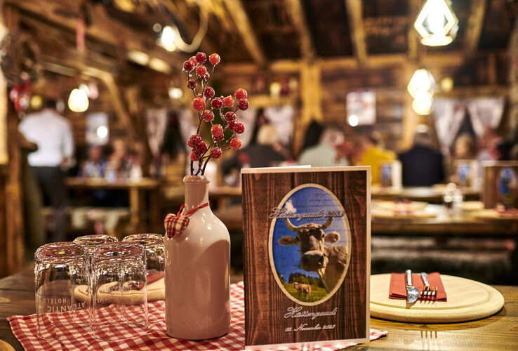 Gemütliche Hotelrestaurant-Szene mit rustikalem Dekor, roter Tischdecke, Vase mit Beeren und Speisekarte im Vordergrund.