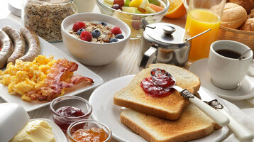 Rich breakfast buffet with toast, jam, scrambled eggs, sausages, fruit, muesli, coffee and orange juice.