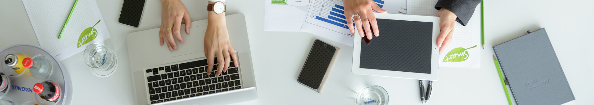 Tagungstechnik für Ihre Veranstaltung im ATLANTIC Hotel Galopprennbahn Zwei Personen arbeiten an einem Tisch mit Laptop, Tablet, Notizblöcken und Getränken im ATLANTIC Hotel Galopprennbahn.