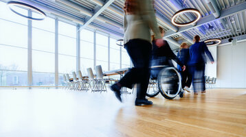 Heller Konferenzraum im ATLANTIC Hotel Universum, mit großen Fenstern, modernen Leuchten und Menschen in Bewegung.