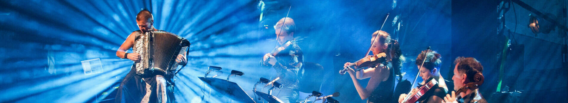 Konzert Kimmo Pohjonen und Kammerphilharmonie Orchester Lübeck | ATLANTIC Grand Hotel Travemünde Musiker auf Bühne mit Akkordeon und Streichern, umgeben von blauem Licht und Strahlen.