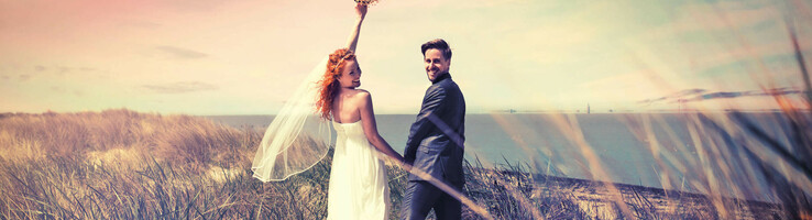 Bride and groom on the beach with a view of the sea, woman lifts a bouquet of flowers, romantic atmosphere.