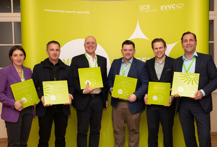 Six people holding awards in front of a green background at an awards ceremony.