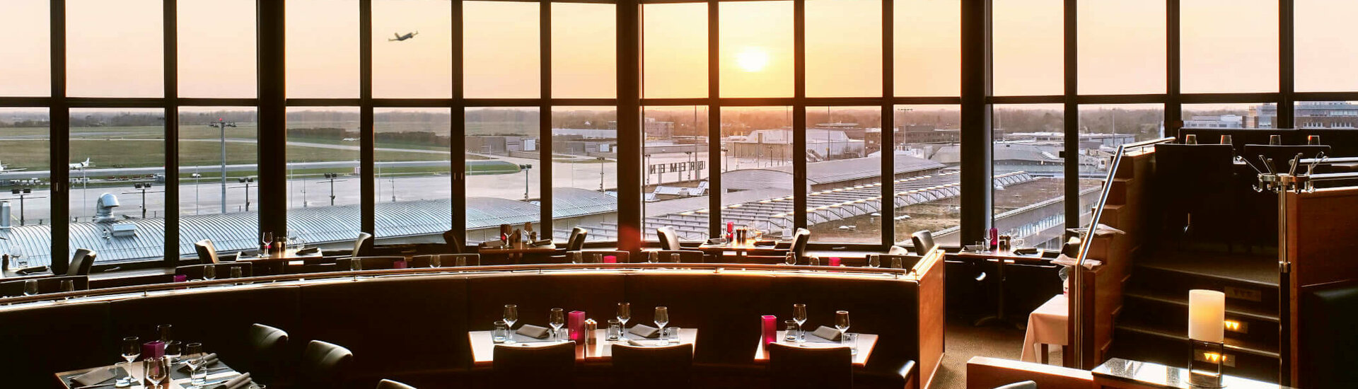 Restaurant Blixx im ATLANTIC Hotel Airport in Bremen Restaurant mit Panoramafenstern, Blick auf Flughafen und Sonnenuntergang, elegant gedeckte Tische im ATLANTIC Hotel Airport Bremen.