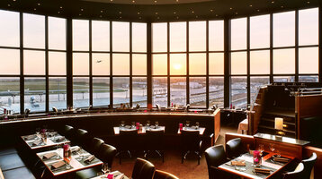 Restaurant with panoramic windows, view of the airport and sunset, elegantly laid tables at the ATLANTIC Hotel Airport Bremen.