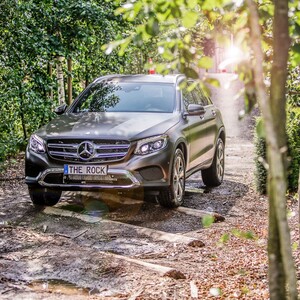 Mercedes Benz Geländewagen auf dem Parcours "The Rock" SUV fährt auf einem Waldweg, umgeben von Bäumen und Sonnenlicht.