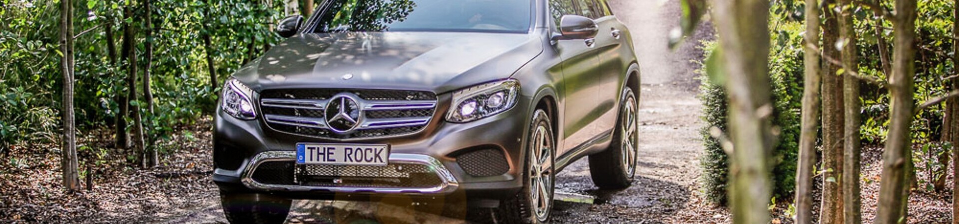 Mercedes Benz Geländewagen auf dem Parcours "The Rock" SUV fährt auf einem Waldweg, umgeben von Bäumen und Sonnenlicht.