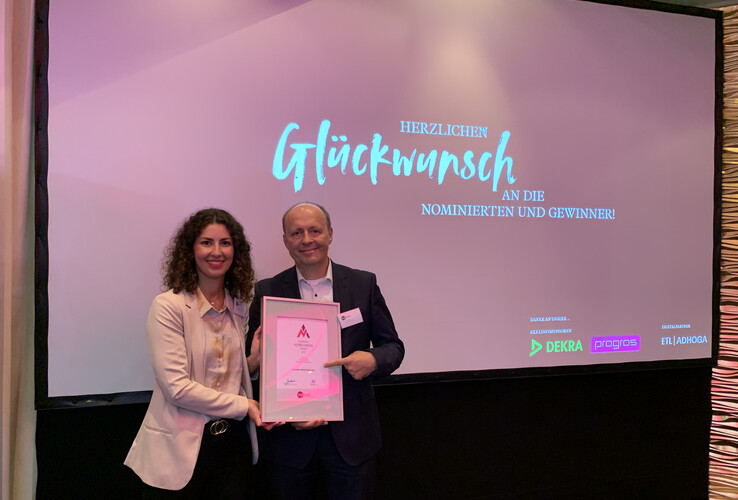 Two people holding a certificate in front of a screen with "Congratulations" at the ATLANTIC Hotel Münster.
