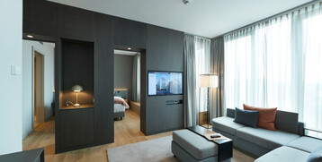 Modern hotel room at the ATLANTIC Grand Hotel Bremen with sofa, flat-screen TV and large windows with curtains.