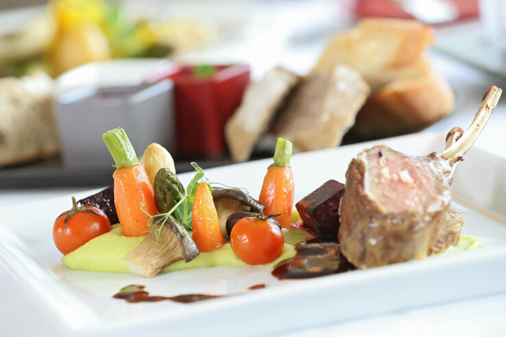 Gourmetgericht mit Lammkarree, buntem Gemüse und Sauce kunstvoll auf weißem Teller im ATLANTIC Grand Hotel Travemünde.