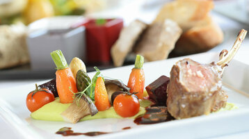 Restaurant Holstein's Gourmet dish with rack of lamb, colorful vegetables and sauce artfully served on a white plate at the ATLANTIC Grand Hotel Travemünde.