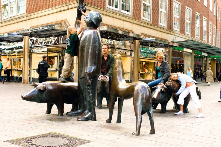 Children and adults play on bronze sculptures of pigs in a busy Sögestraße in Bremen.