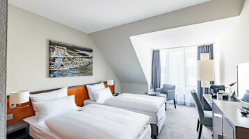 ATLANTIC Hotel Vegesack Superior Double Room Bright hotel room with two single beds, desk, armchair and large window.