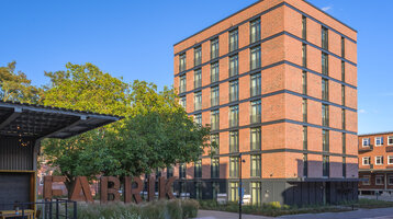 Rotes Backsteinhotel mit mehreren Etagen, umgeben von Bäumen, bei klarem Himmel.