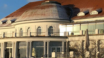 Historische Hotelarchitektur mit rotem Dach, umgeben von schneebedecktem Garten unter klarem, blauem Himmel.