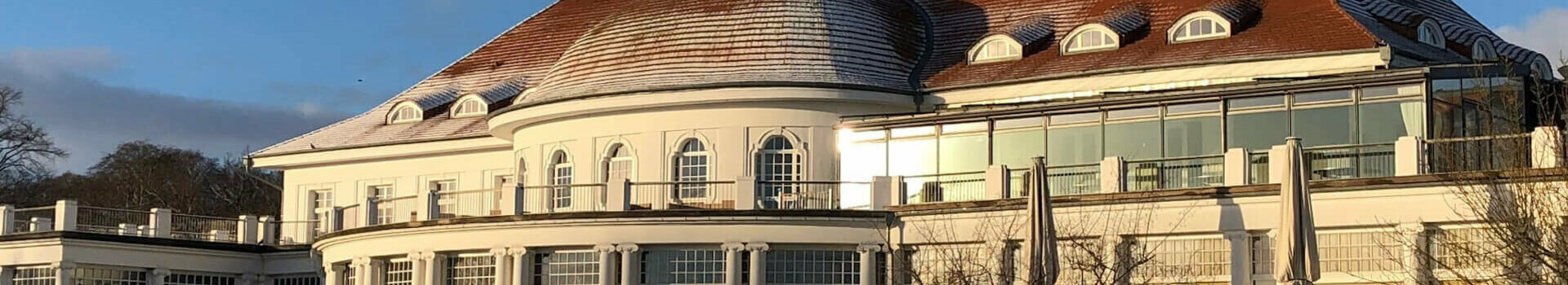 Außenaufnahme des ATLANTIC Grand Hotels Travemünde im Winter Historische Hotelarchitektur mit rotem Dach, umgeben von schneebedecktem Garten unter klarem, blauem Himmel.