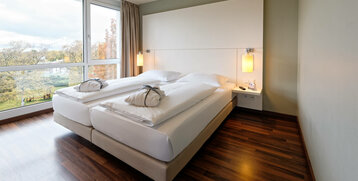 Bright hotel room with double bed, wooden floor and large window with a view of the greenery at the ATLANTIC Hotel Galopprennbahn.