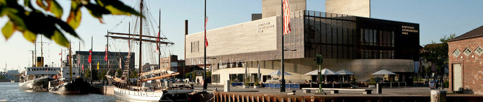 Harbor view in Bremerhaven with sailing ship and modern building on the shore at sunset.