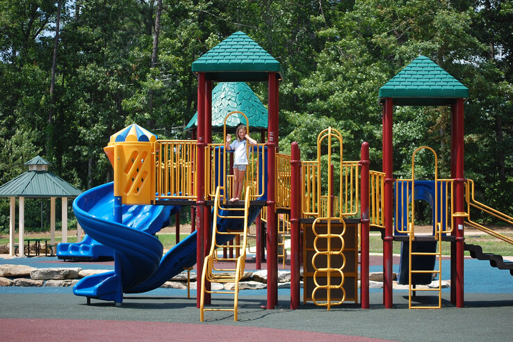 Spielplatz mit buntem Klettergerüst und Rutsche, umgeben von Bäumen.